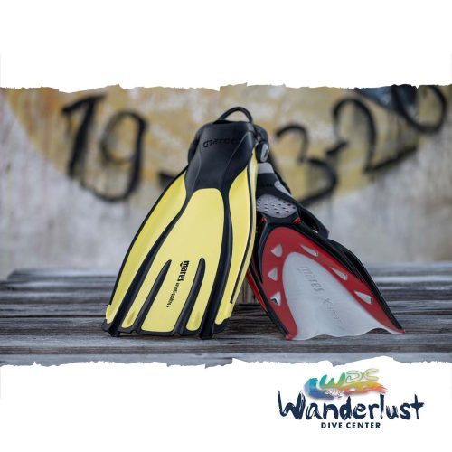 Yellow and red scuba fins resting on driftwood near a Bonaire shore entry