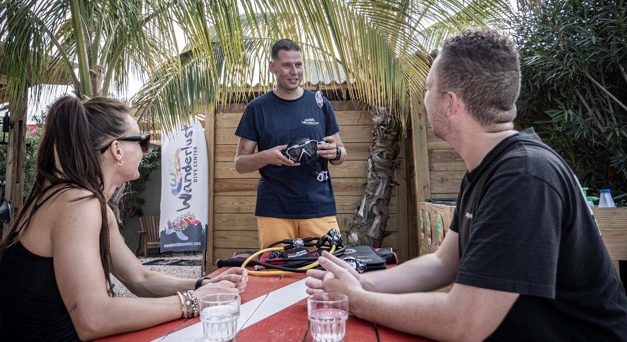header-get-certified Stephan from Wanderlust Dive Center giving a personal dive briefing to guests under palm trees on Bonaire