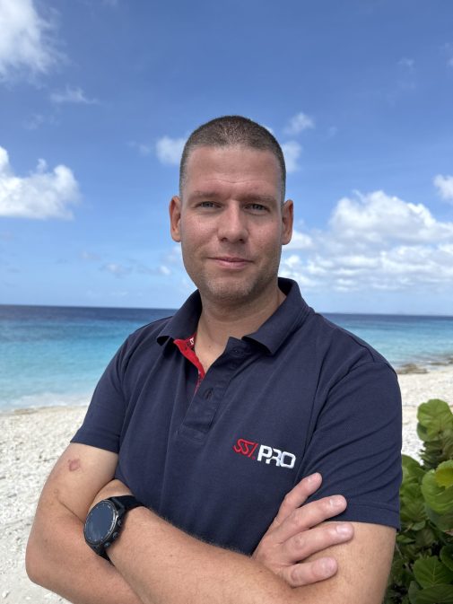 profile-picture-stephan Instructor Trainer Stephan standing on a sandy beach with blue water in the background on Bonaire